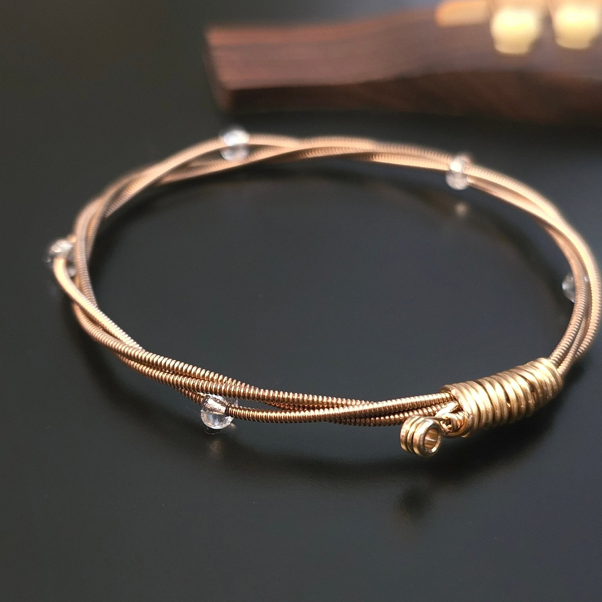 bronze coloured guitar string bangle bracelet with clear glass beads on a black guitar