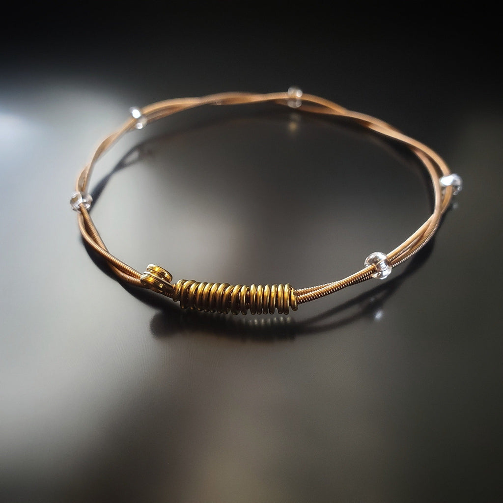 bronze coloured bangle style guitar string bracelet with clear glass beads with black background