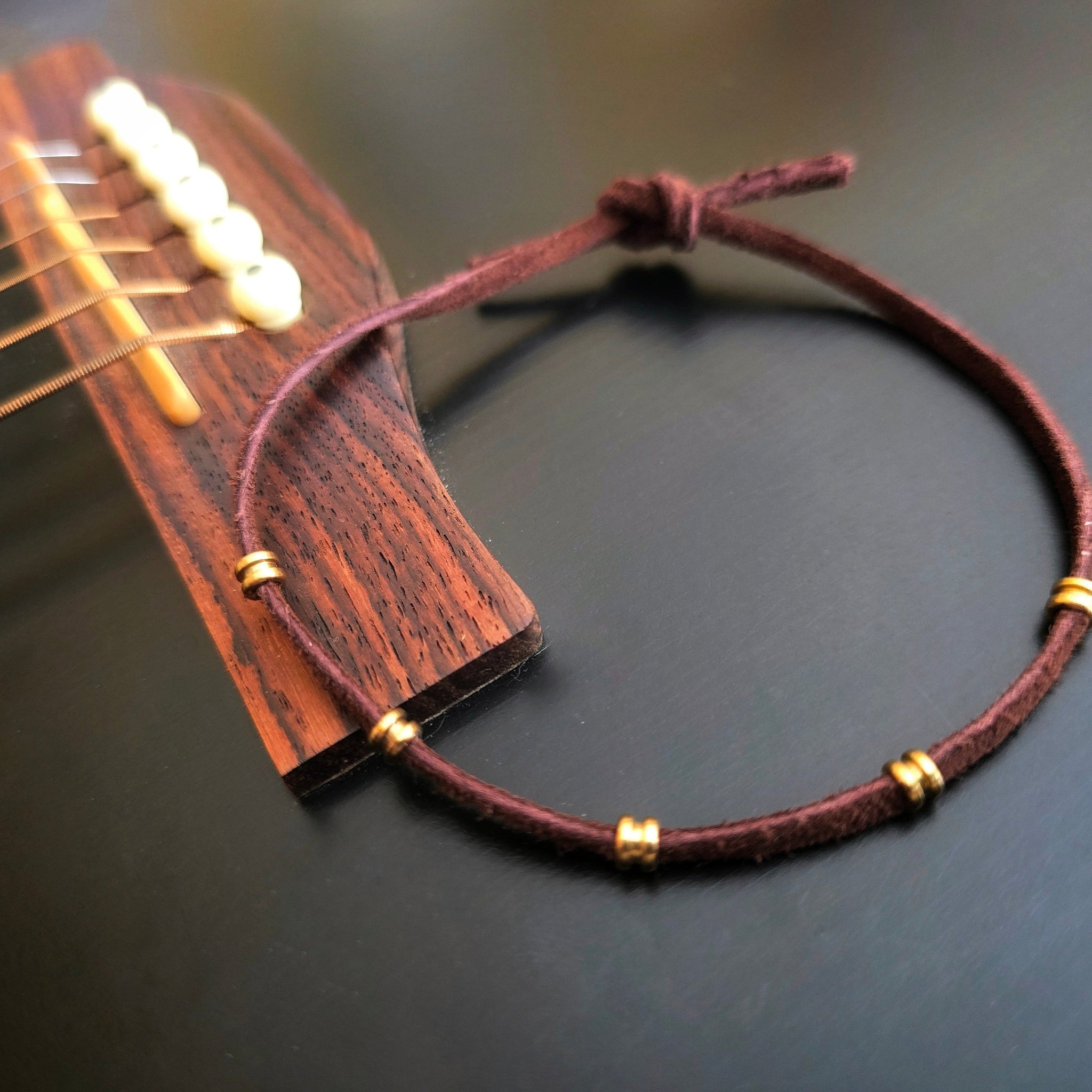 brown suede and guitar string ballend bracelet on a black guitar