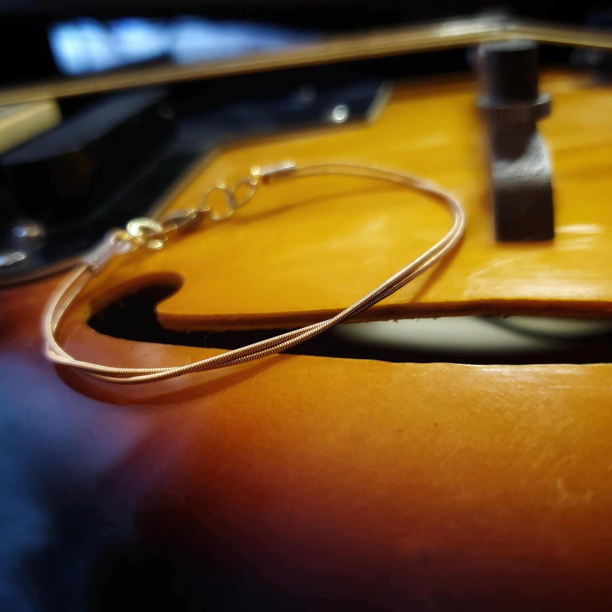 clasp style bracelet made from an upcycled mandolin string sitting over the F hole of a gold coloured mandolin