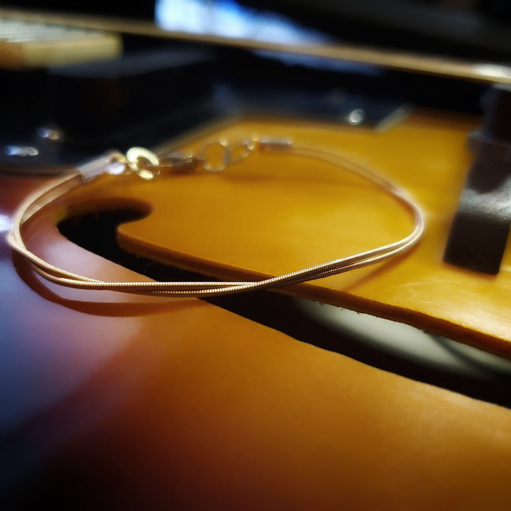 clasp style bracelet made from an upcycled mandolin string sitting over the F hole of a gold coloured mandolin