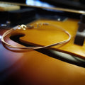 clasp style bracelet made from an upcycled mandolin string sitting over the F hole of a gold coloured mandolin