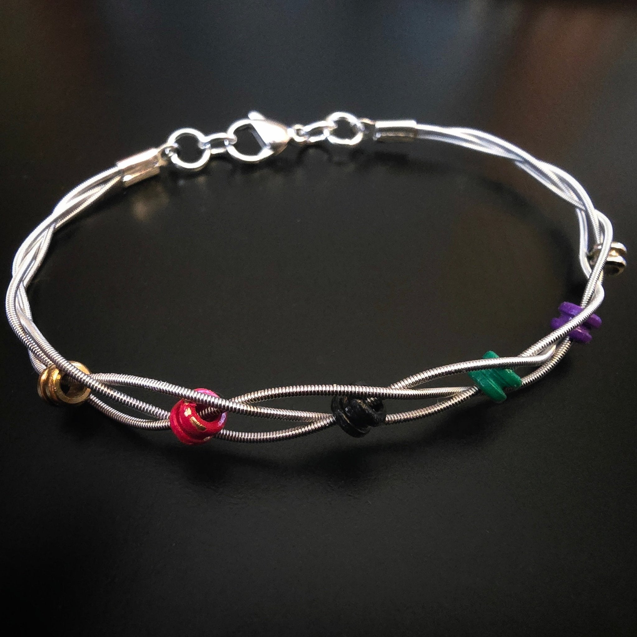guitar string bracelet with six multicoloured ball end beads on black background