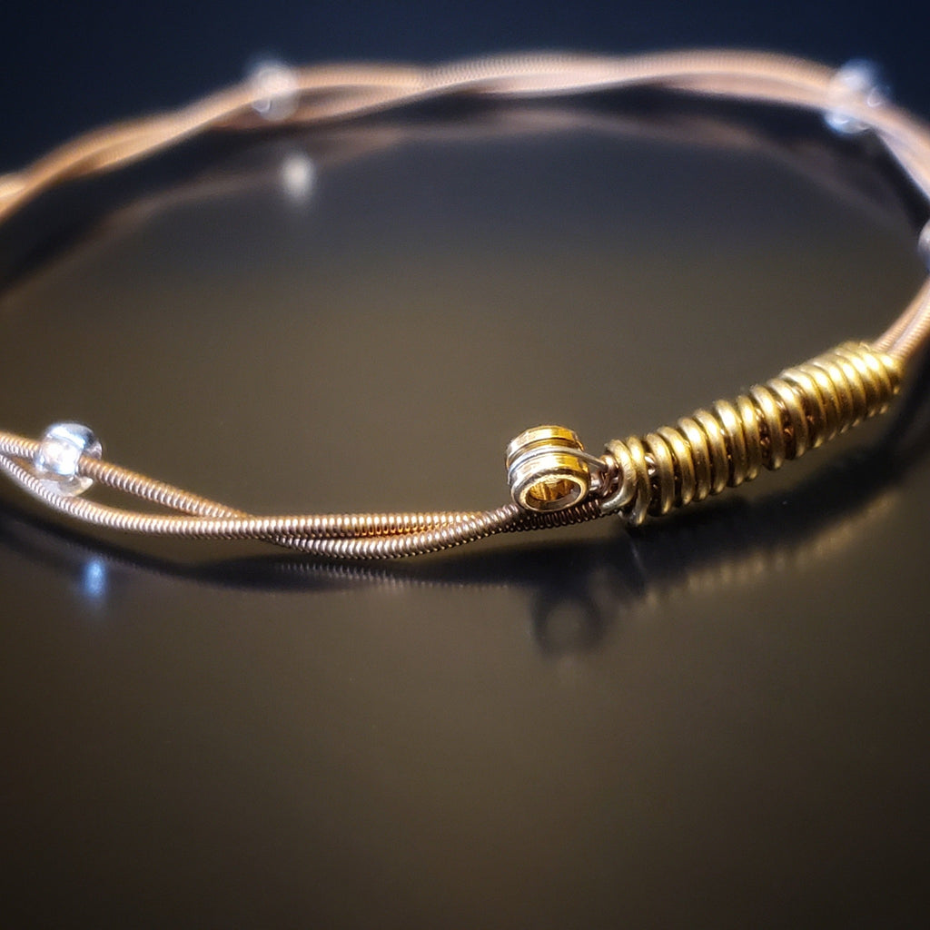 bronze coloured bangle style guitar string bracelet with clear glass beads with black background