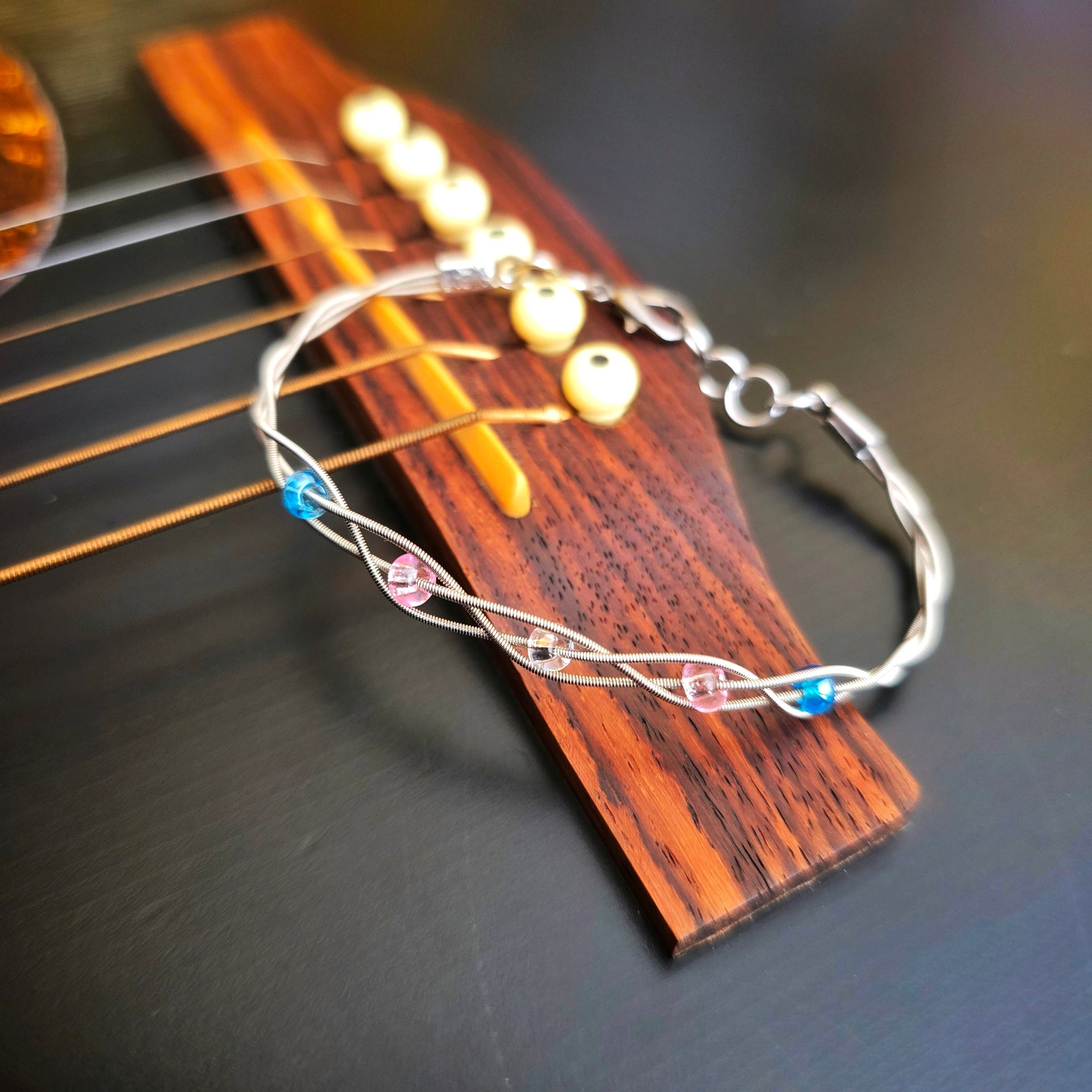 closeup braided trans pride guitar string bracelet on black guitar