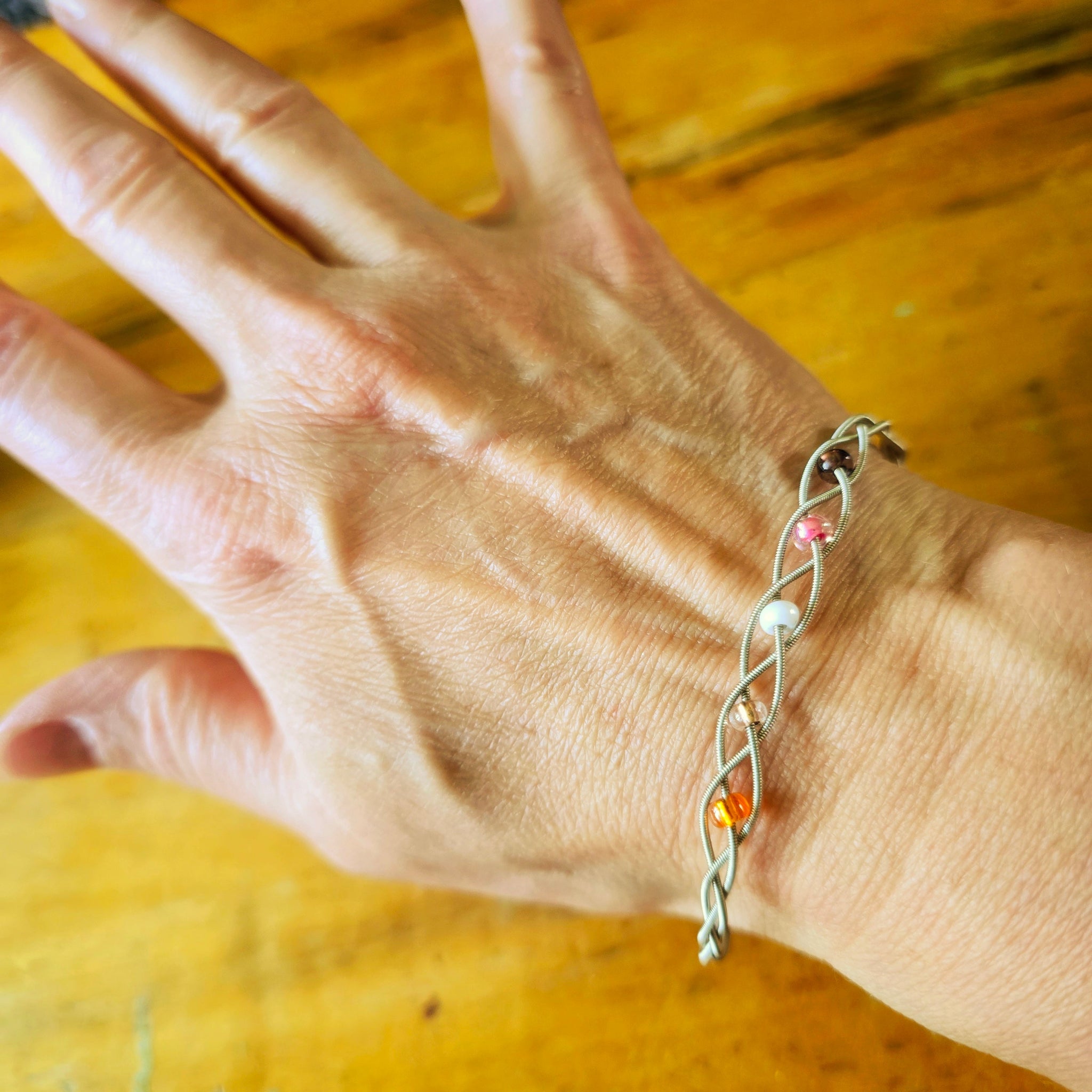 closeup of hand wearing guitar string bracelet with 5 beads representing the colours of the lesbian pride flag 