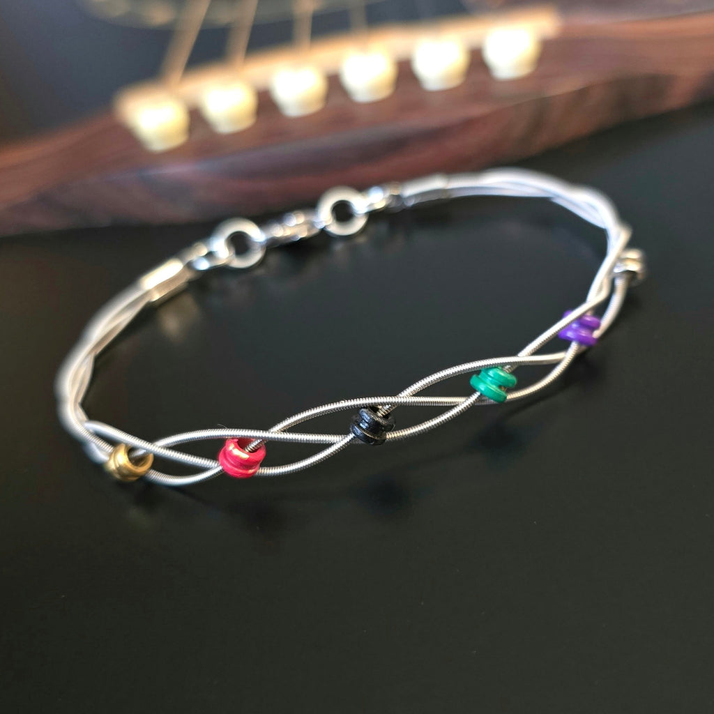 guitar string bracelet with six multicoloured ball end beads on bridge of black guitar