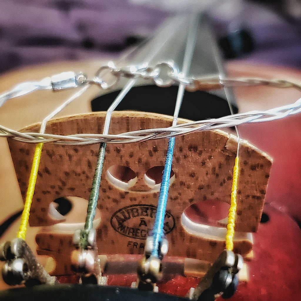 closeup of silver coloured violin string bracelet sitting on a violin bridge