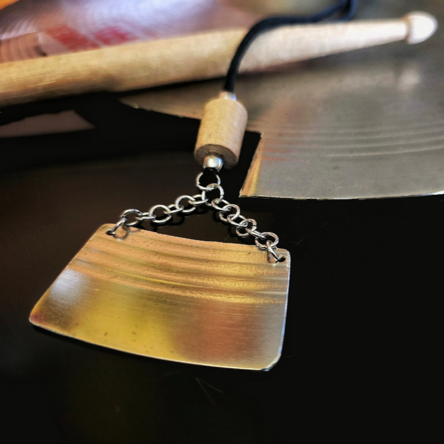 cymbal piece and drumstick black suede necklace sitting on drumstick and cymbal