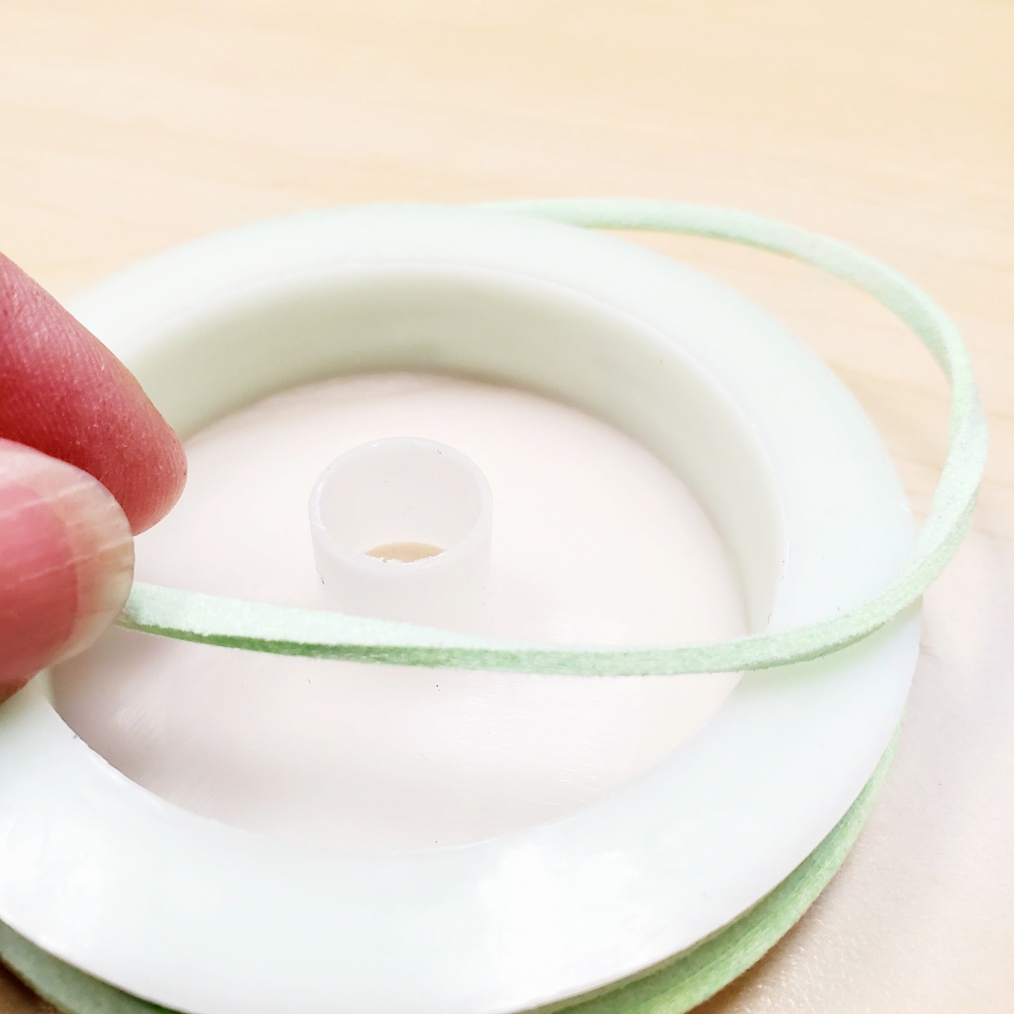 fingers holding a string of lime green faux-suede coming from a white bobbin