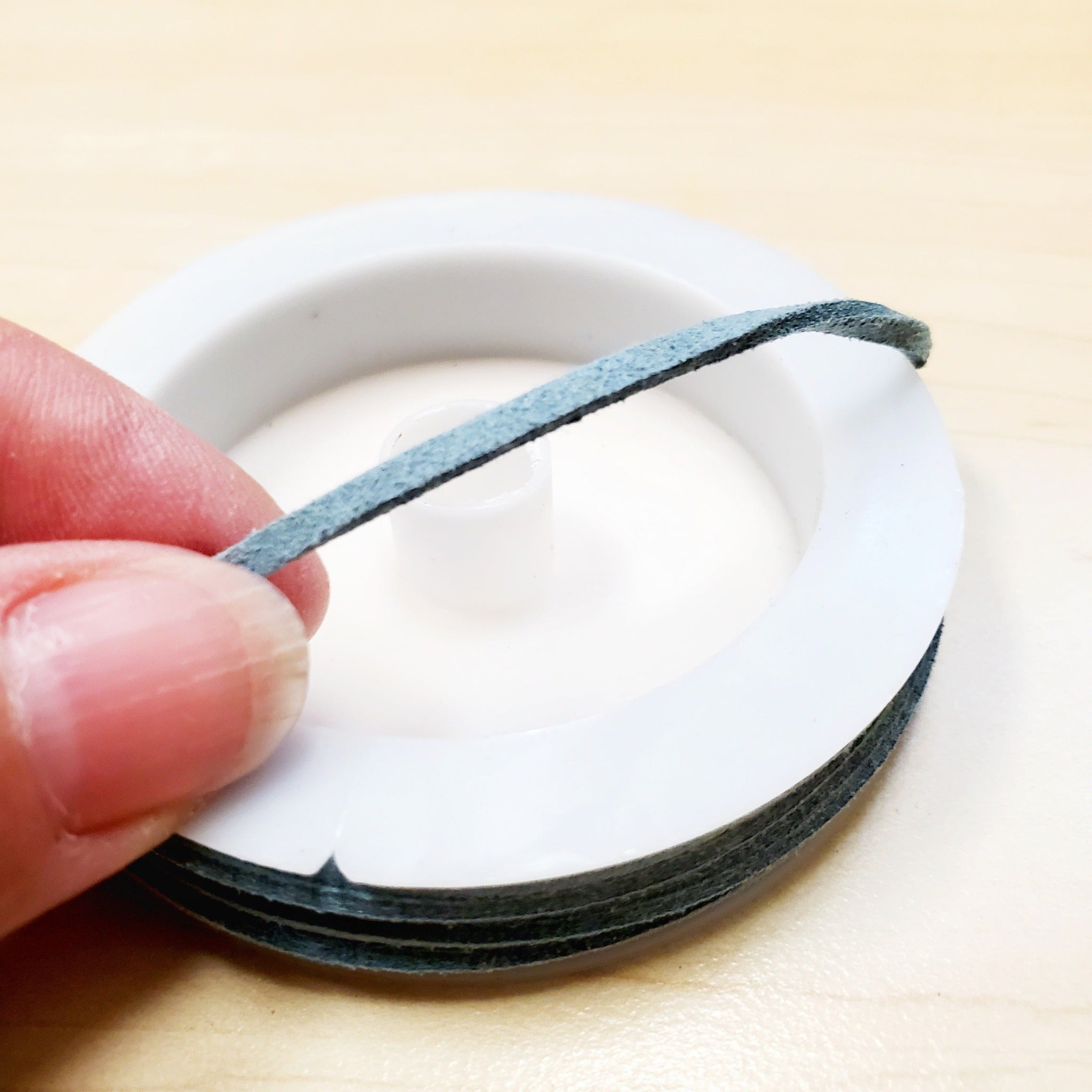 fingers holding a string of sage green faux-suede coming from a white bobbin