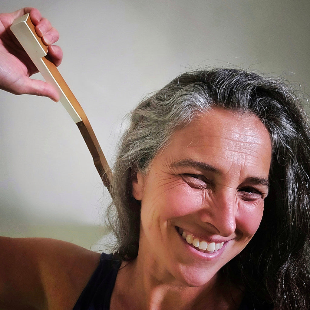 front view of smiling woman using an upcycled piano key backscratcher
