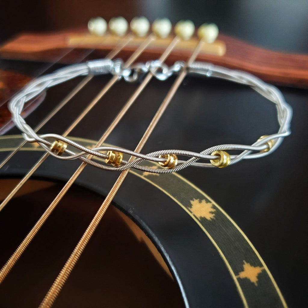 bracelet fait avec 3 brins de cordes de guitare de couleur argent et 5 embouts de cordes de guitare de couleur or sur une guitare noire