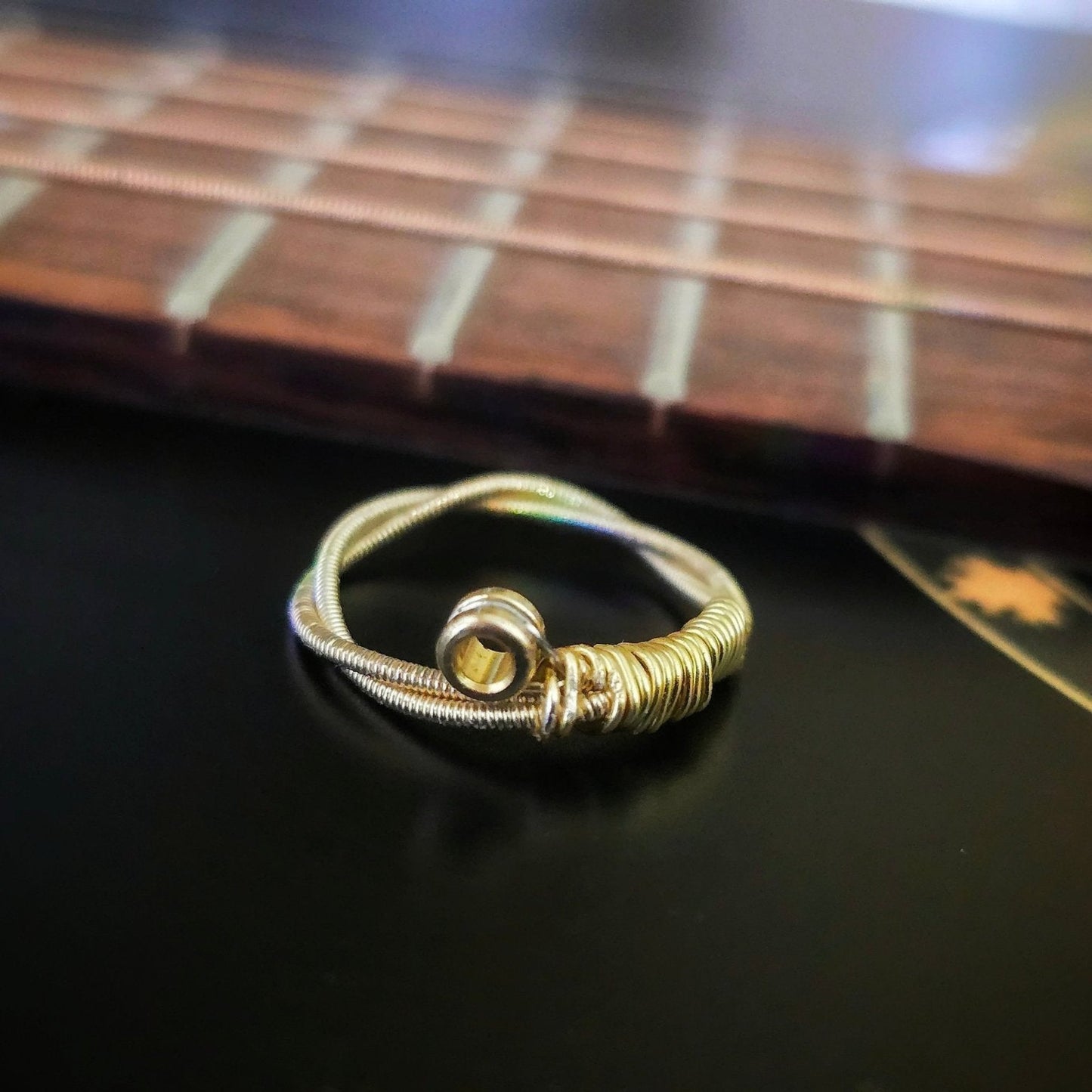 gold coloured upcycled guitar string ring sitting in front of the neck of a black guitar