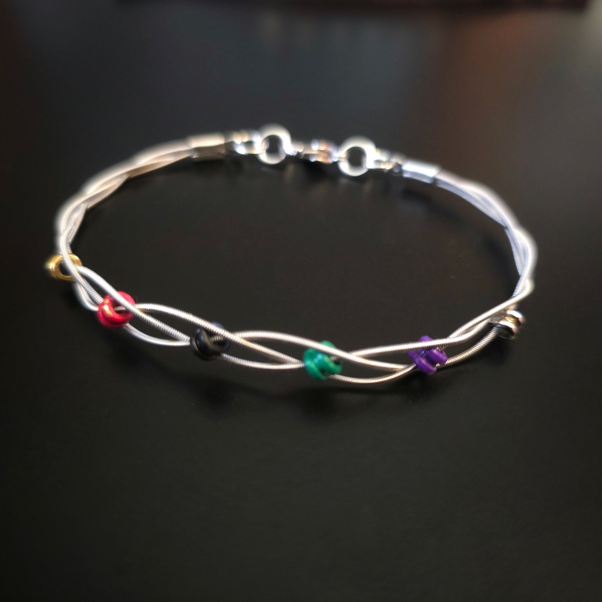 guitar string bracelet with six multicoloured ball end beads on black background