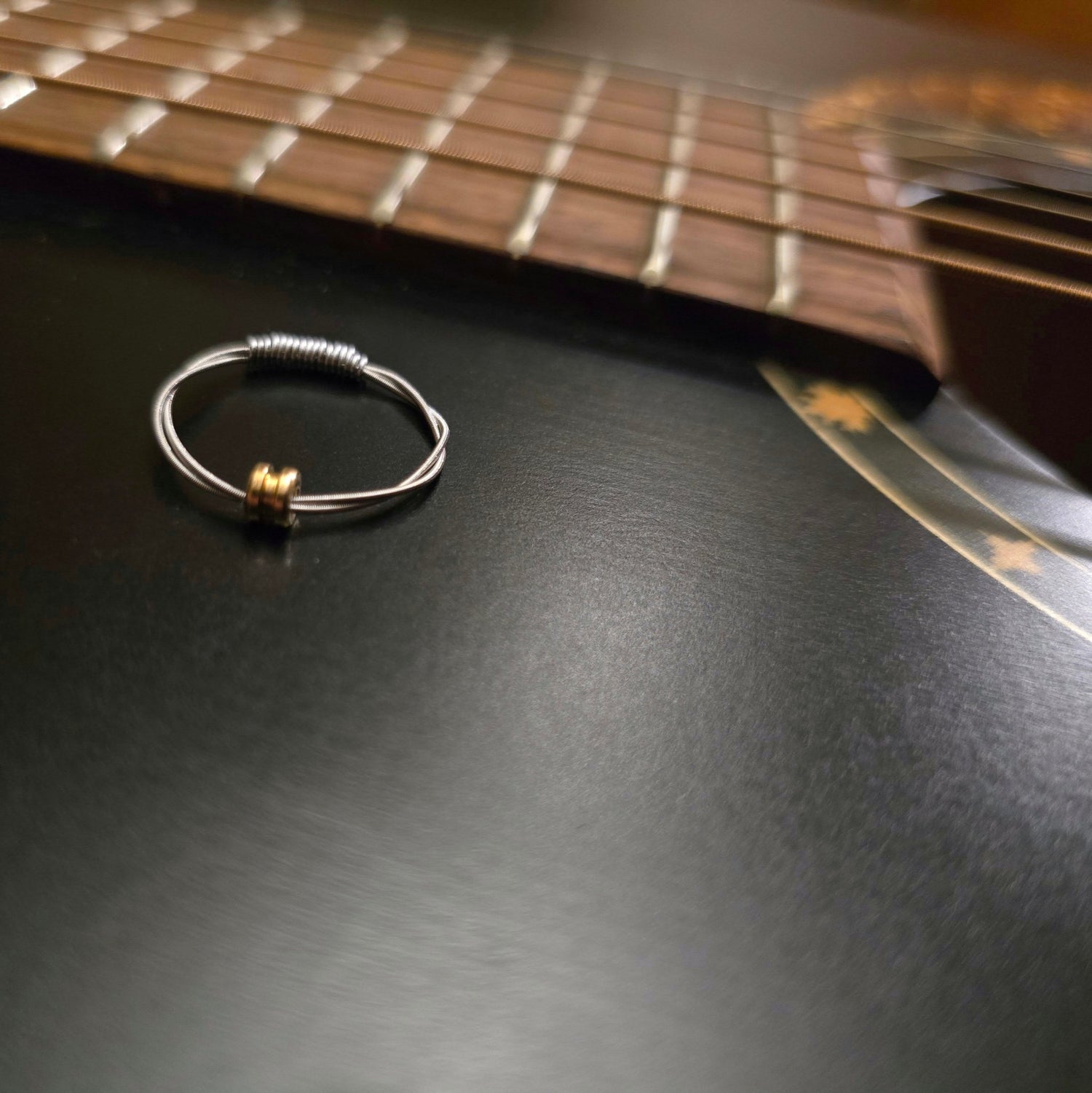 ring made from guitar string and ballend sitting on a black guitar