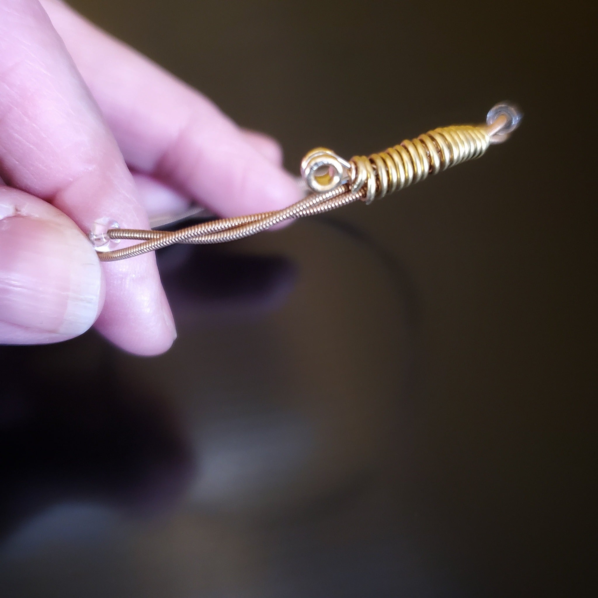 hand holding a bronze coloured bangle style guitar string bracelet with clear glass beads with black background