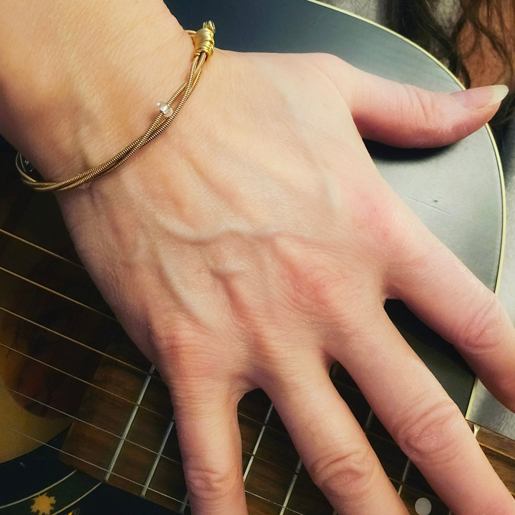 hand on guitar wearing bronze coloured guitar string bangle bracelet with clear glass beads on a guitar