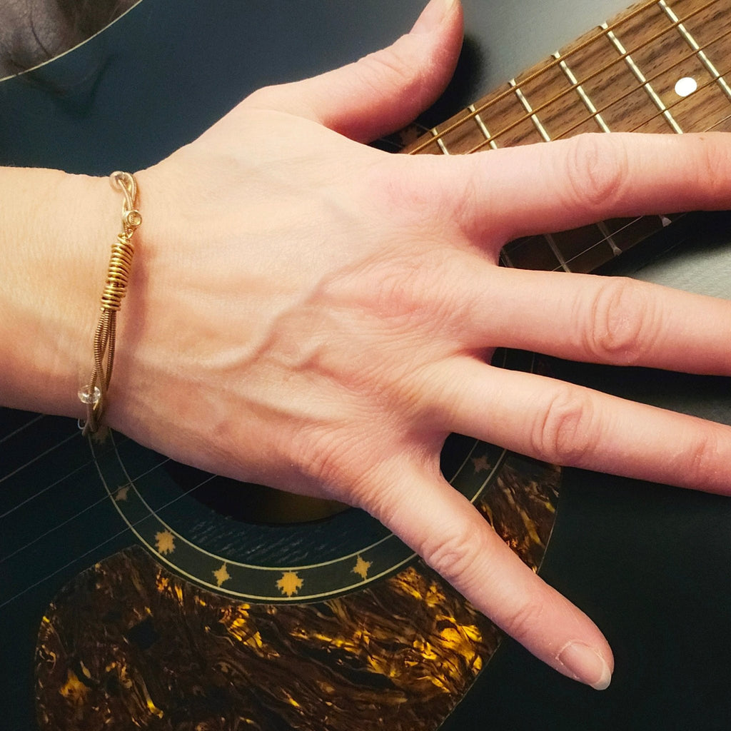 hand on guitar with bronze guitar string beaded bangle bracelet