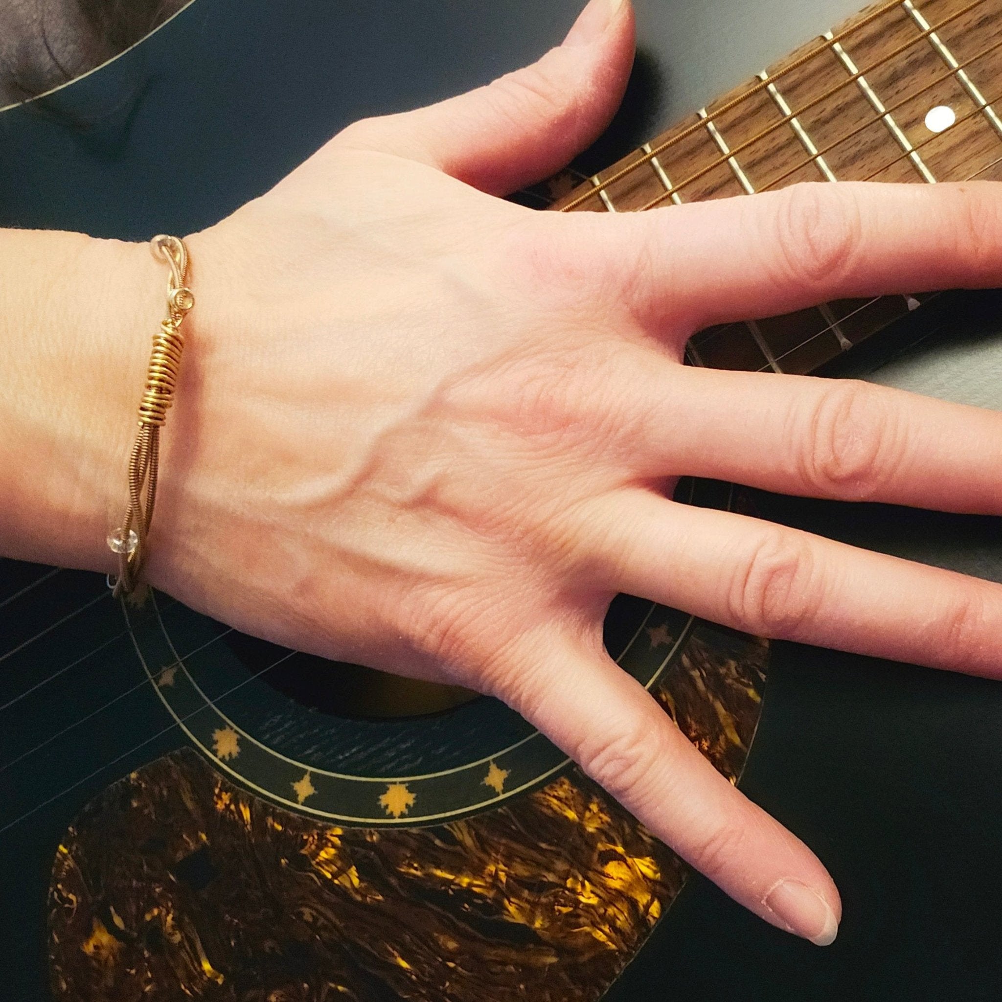 hand on guitar with bronze guitar string beaded bangle bracelet