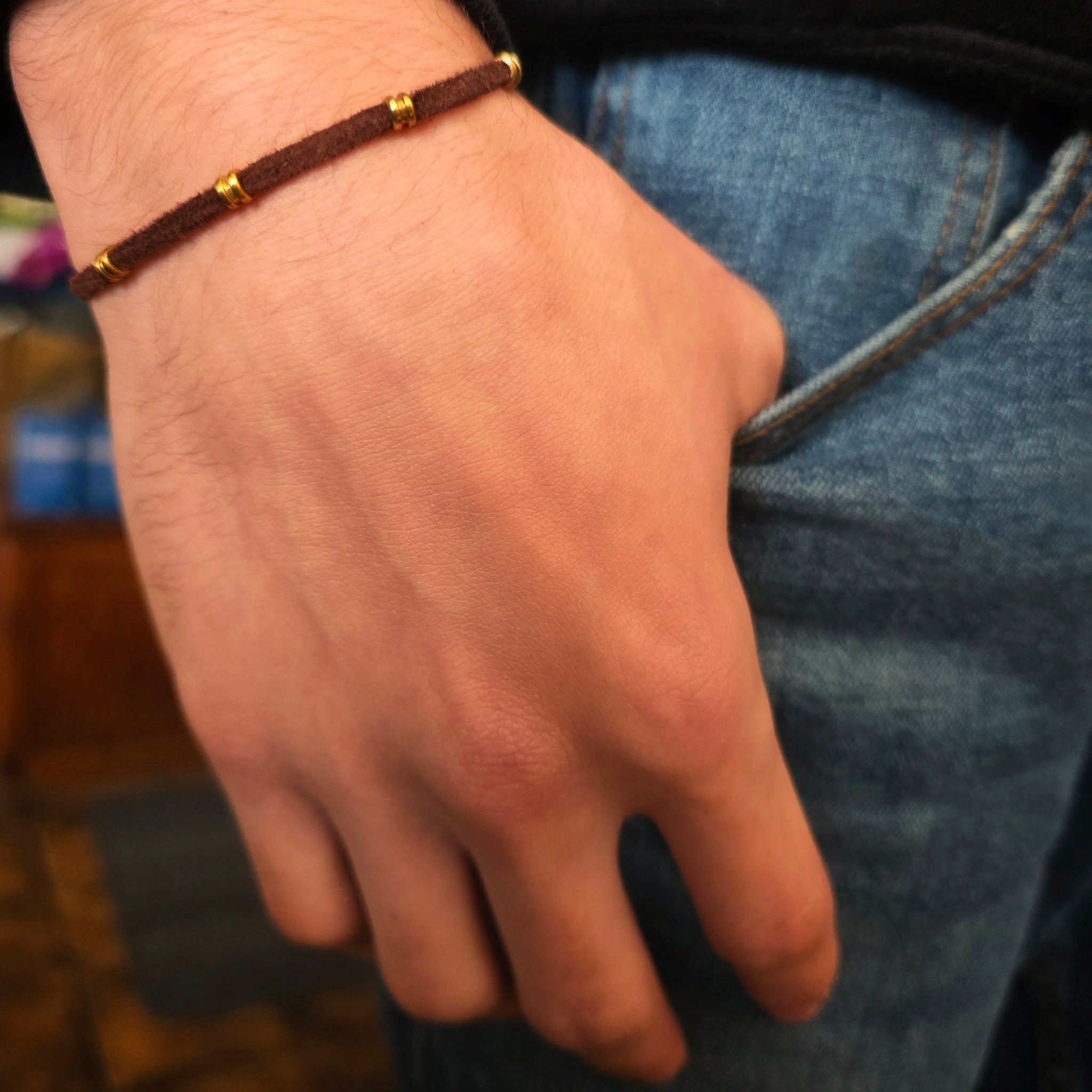 hand with a brown suede and guitar string bracelet with thumb hooked in jean pocked