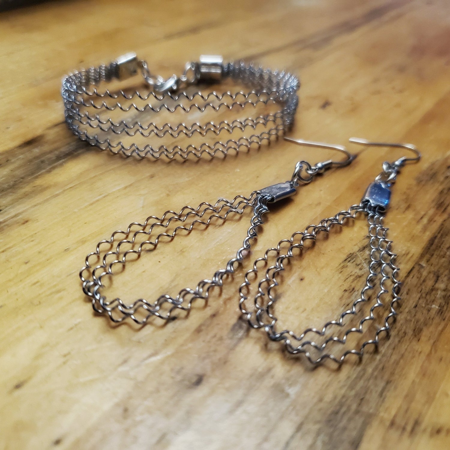 silver coloured bracelet and earrings set made from upcycled snare drum strings on wood grain background