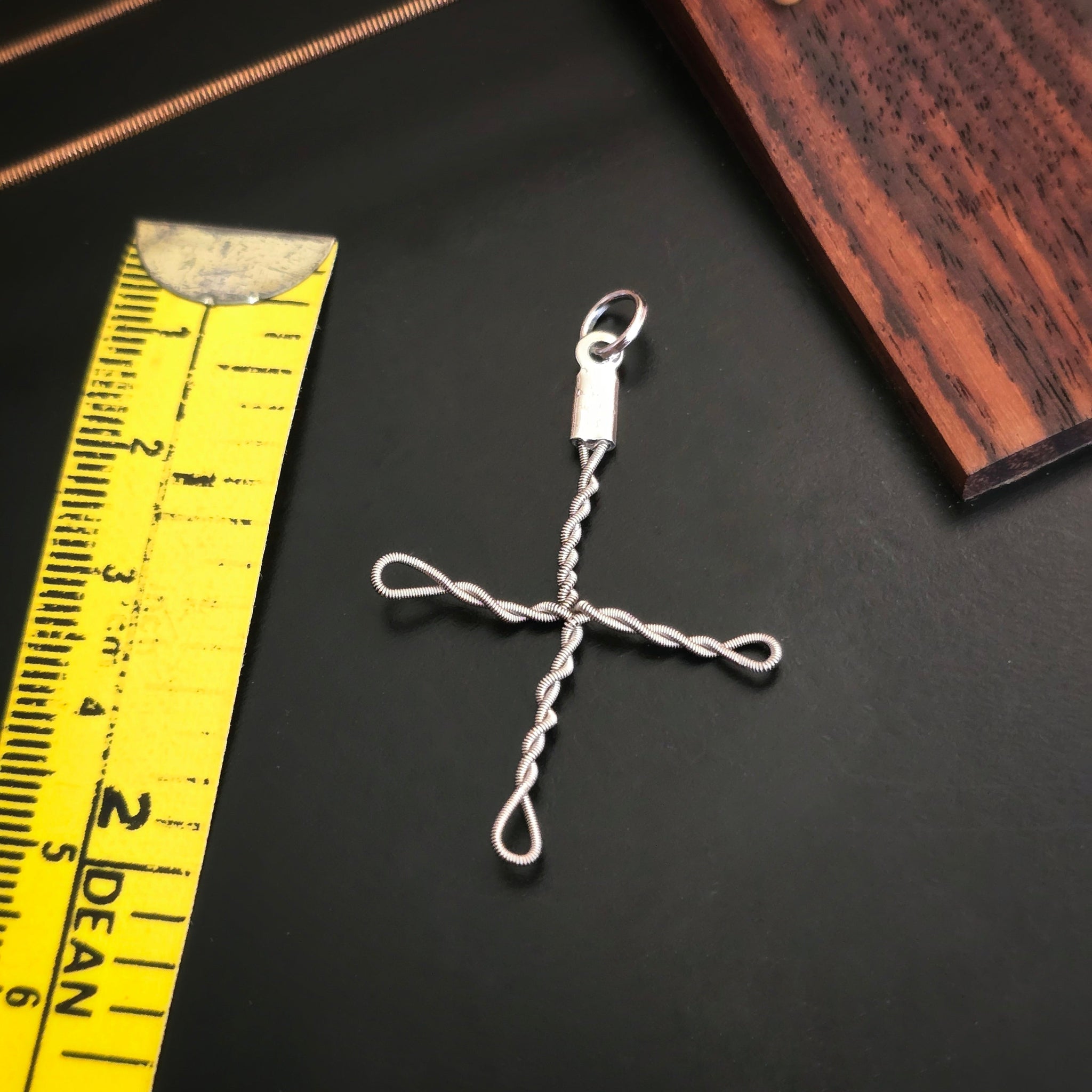 large upcycled guitar string cross style pendant with a yellow measuring tape on a black guitar