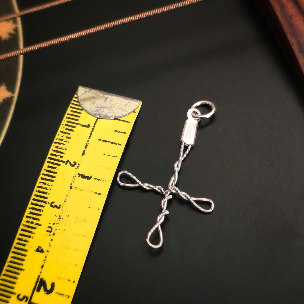 medium upcycled guitar string cross style pendant with a yellow measuring tape on a black guitar