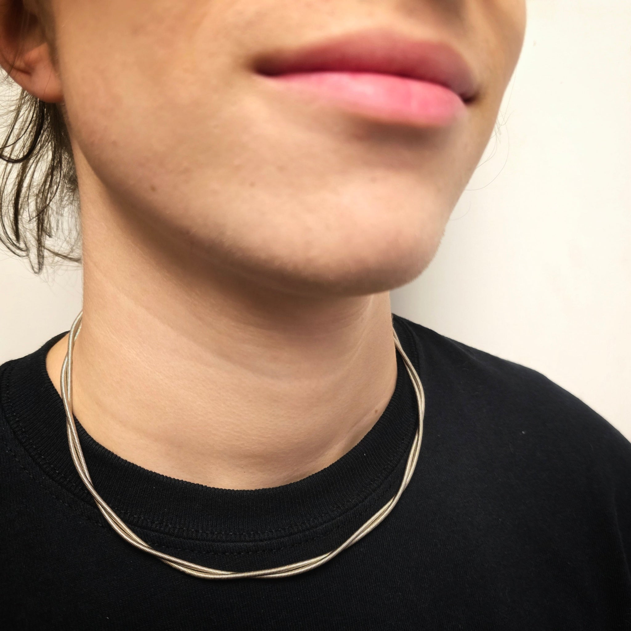 person wearing electric bass guitar string necklace bottom of face and neck with black shirt
