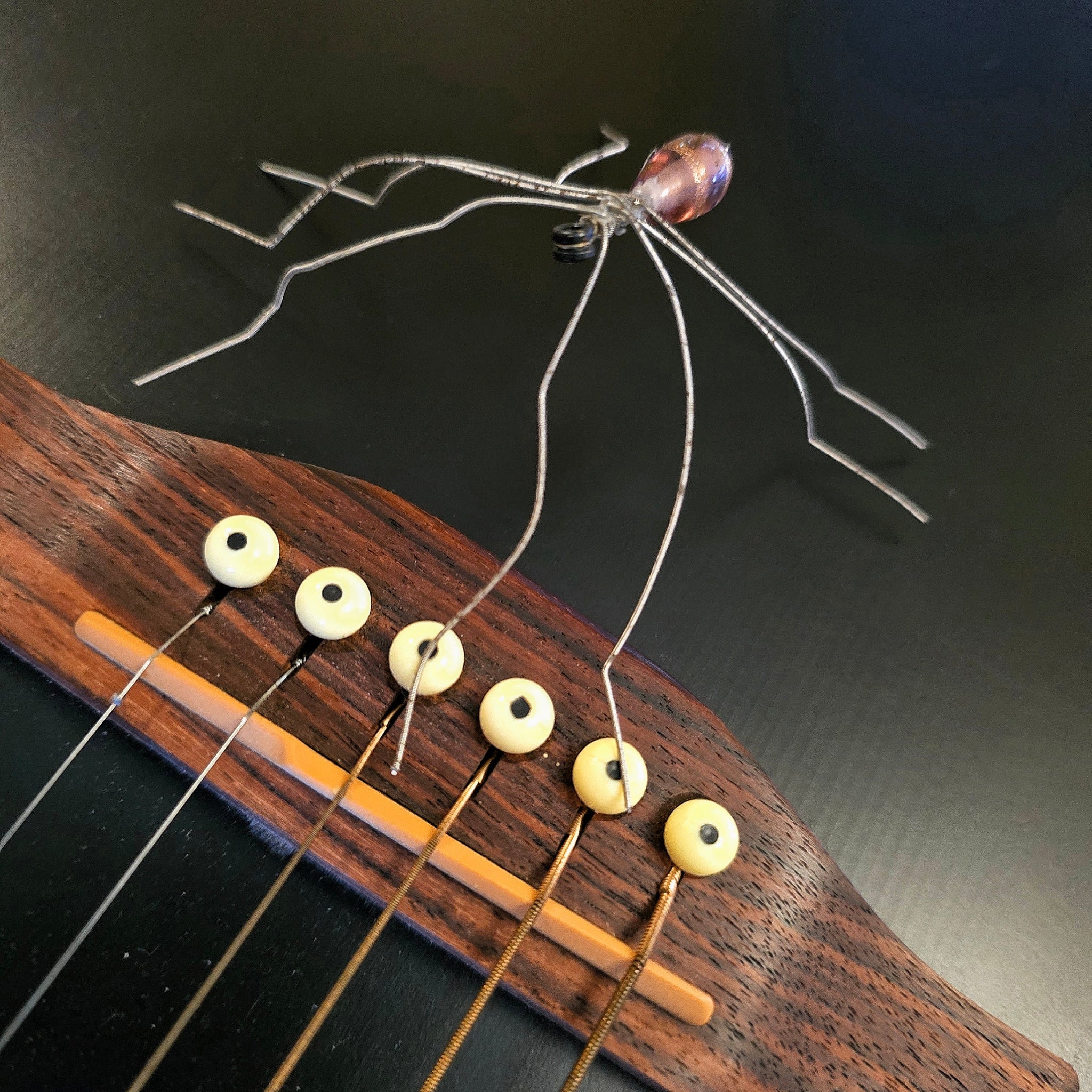 Close-up of a guitar's fretboard with guitar string spider on a dark background
