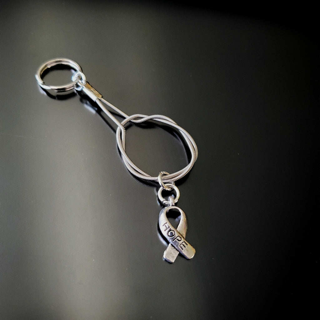 silver coloured keychain made from an upcycled guitar string with a silver coloured ribbon shaped charm with the word HOPE etched on it