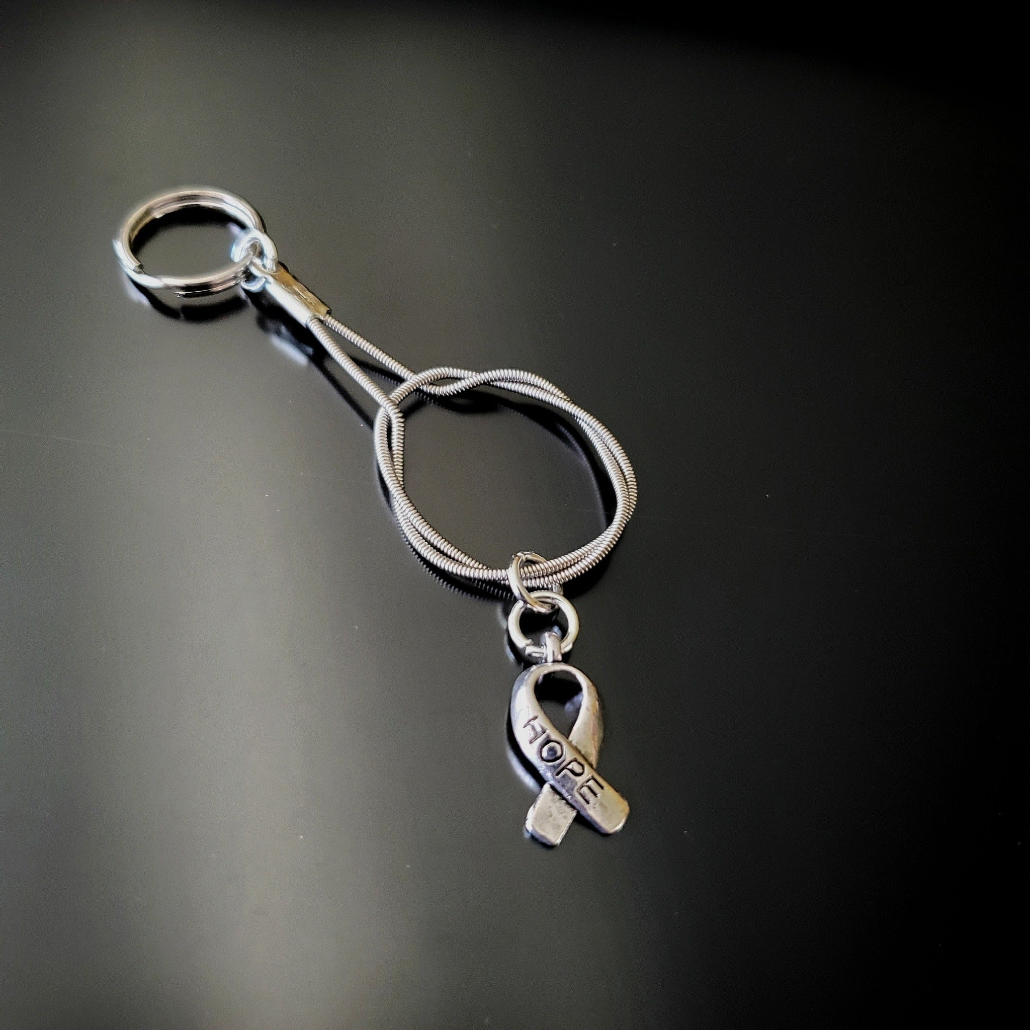 silver coloured keychain made from an upcycled guitar string with a silver coloured ribbon shaped charm with the word HOPE etched on it