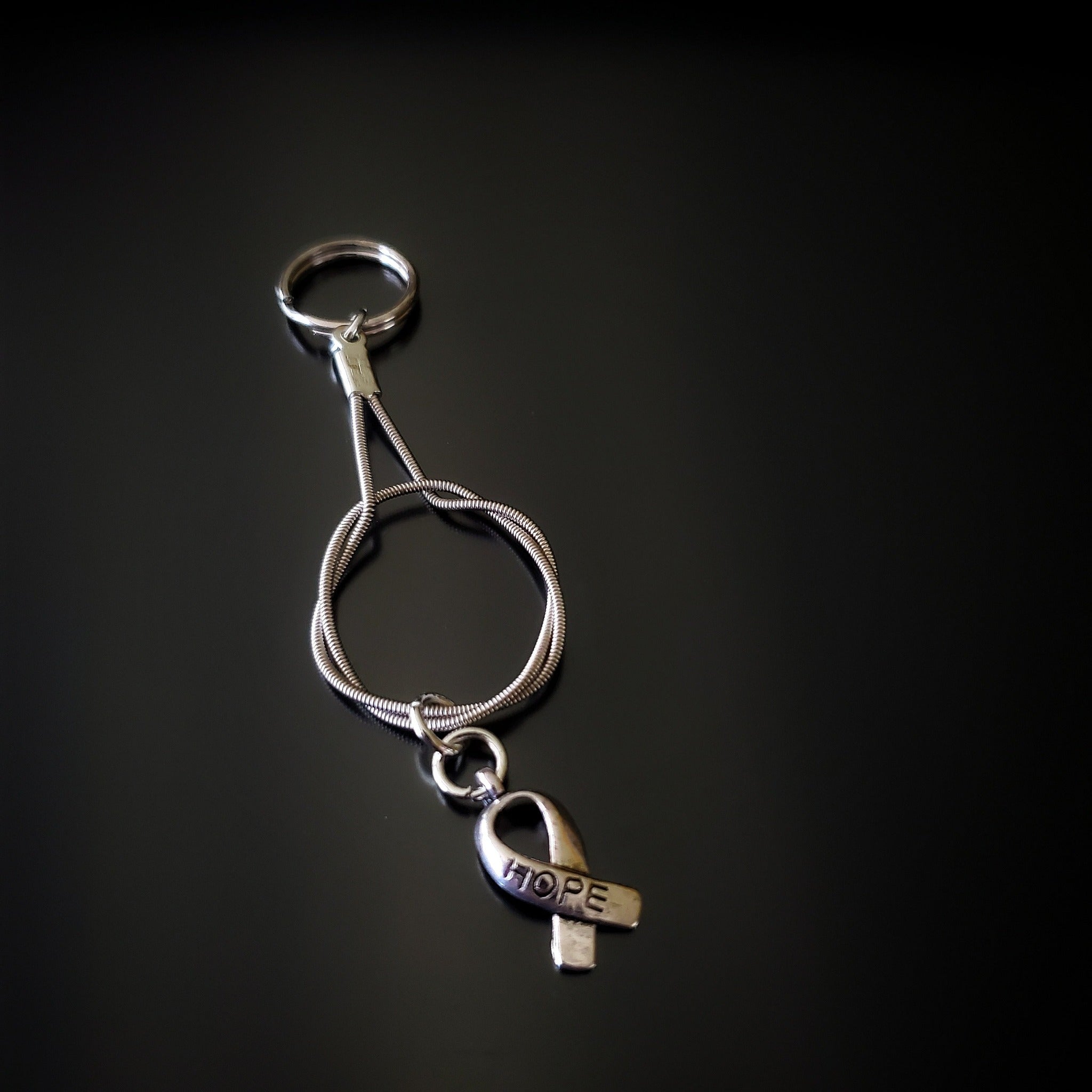 silver coloured keychain made from an upcycled guitar string with a silver coloured ribbon shaped charm with the word HOPE etched on it