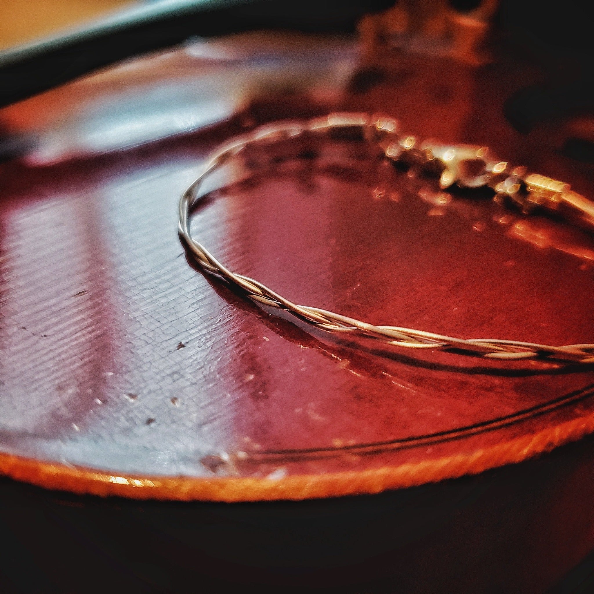 silver coloured violin string bracelet sitting on  the body of a violin
