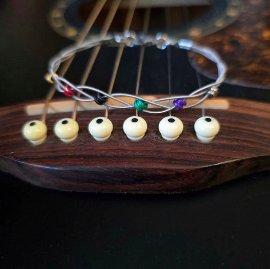 guitar string bracelet with six multicoloured ball end beads on bridge of black guitar