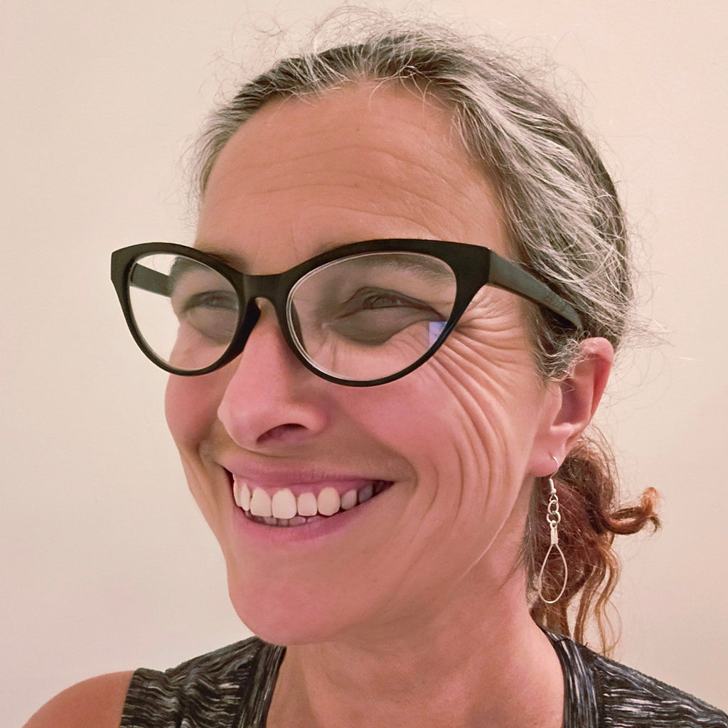 smiling woman in glasses wearing upcycled violin string earrings 