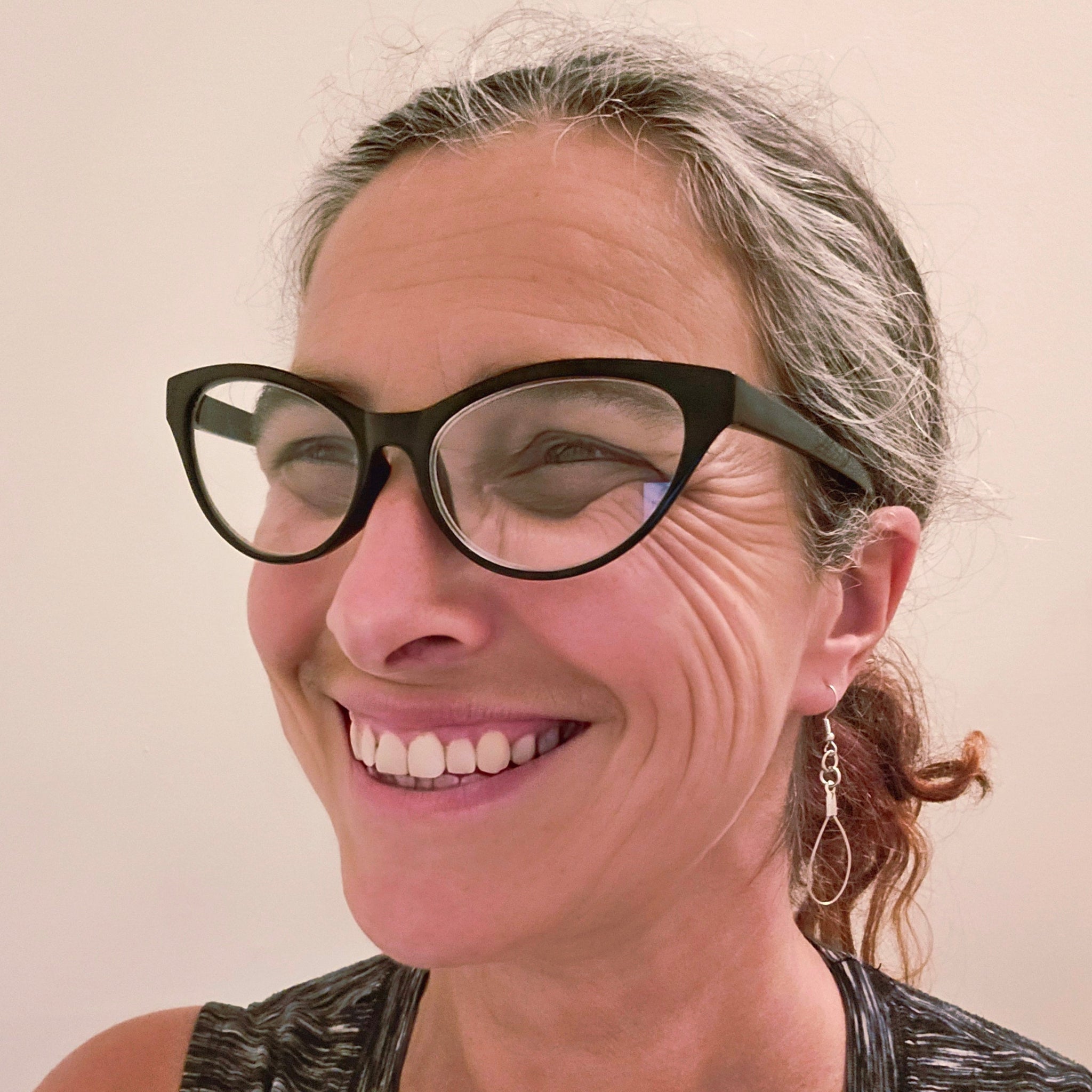 smiling woman in glasses wearing upcycled violin string earrings 