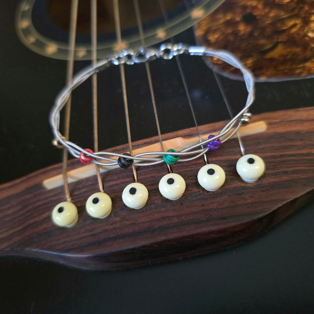 guitar string bracelet with six multicoloured ball end beads on bridge of black guitar