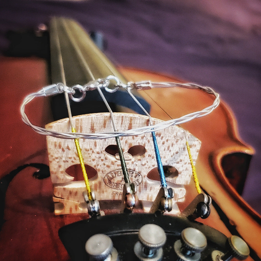 top view silver coloured violin string bracelet sitting on a violin