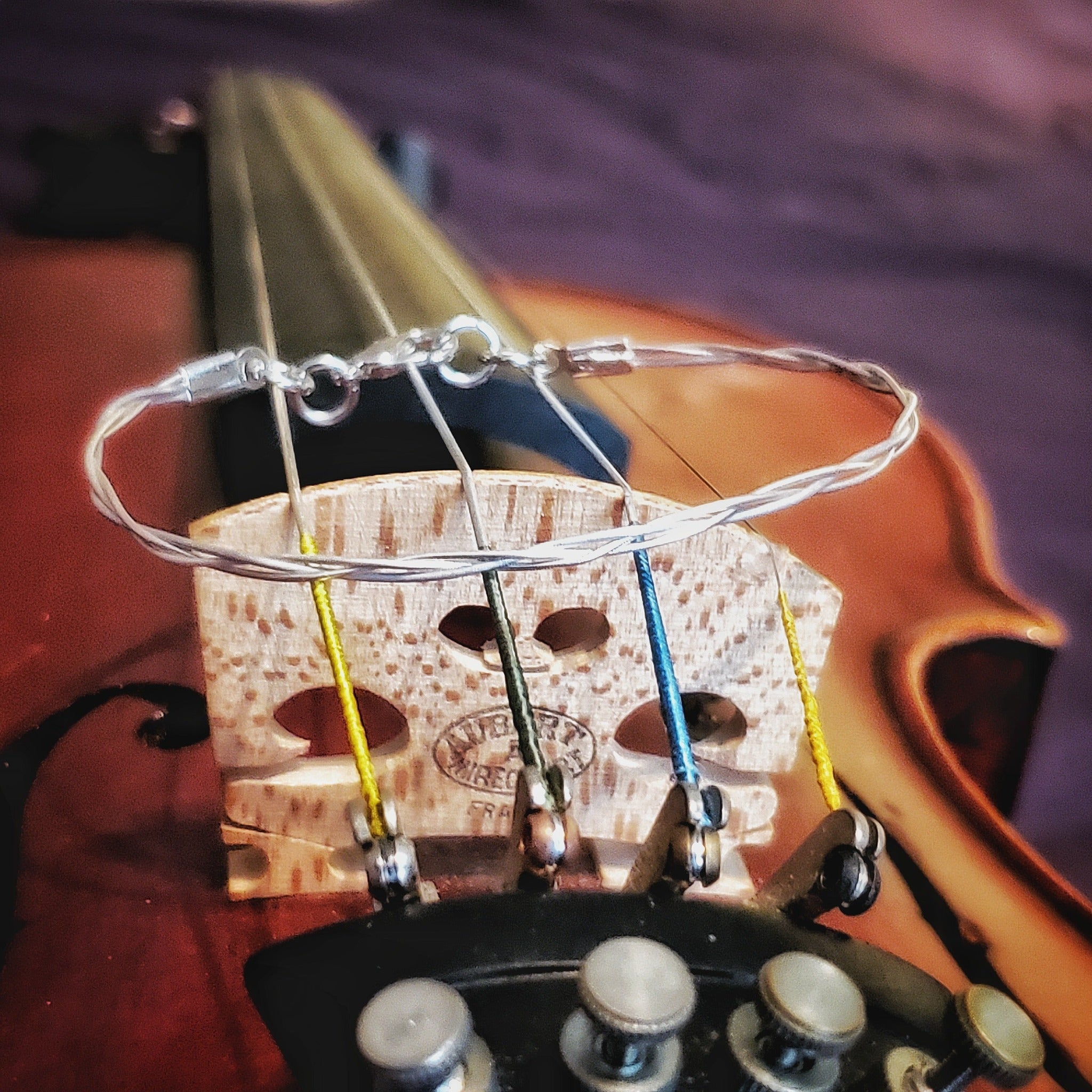 top view silver coloured violin string bracelet sitting on a violin