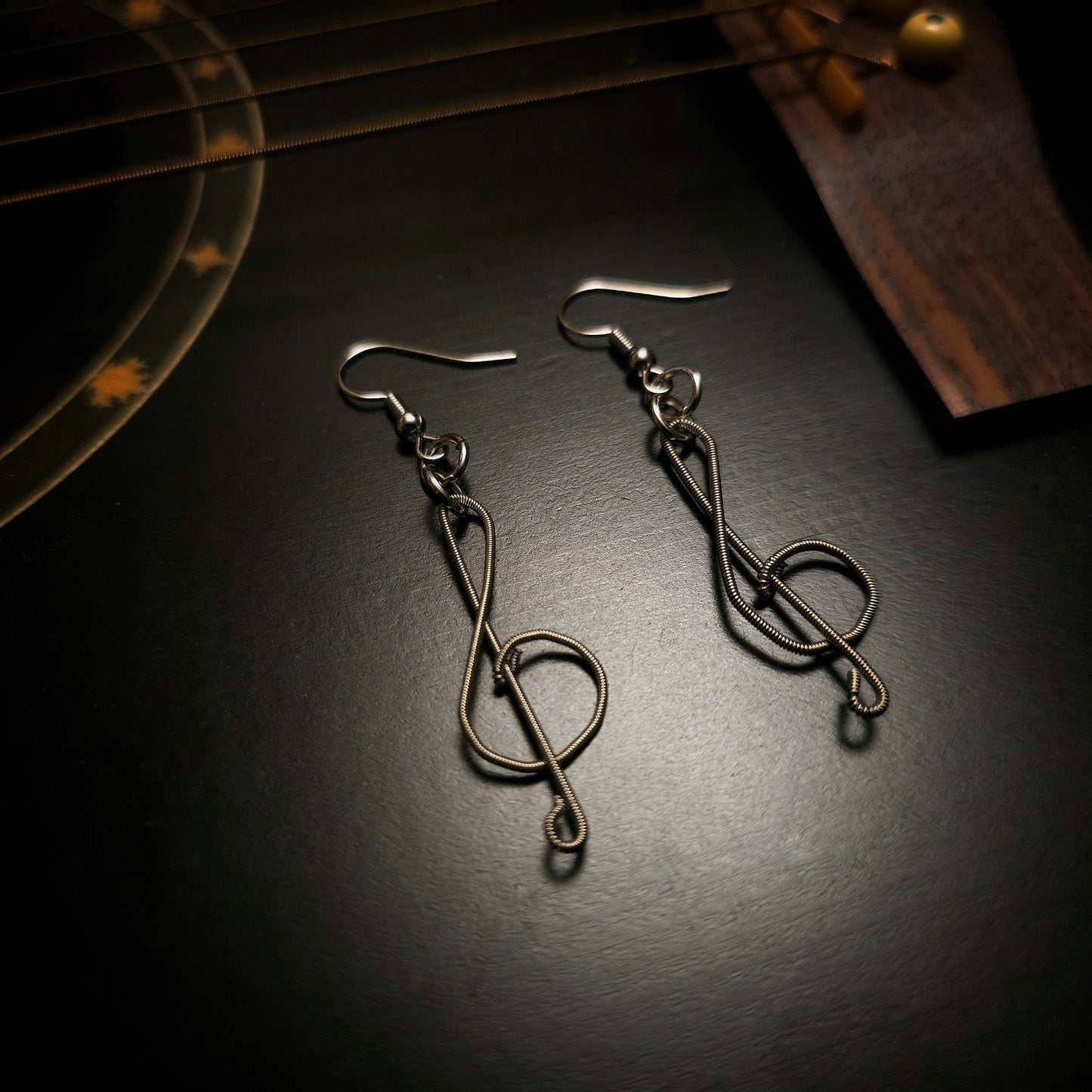 pair of earrings in the shape of treble clefs, made from upcycled guitar strings lying on the body of a black guitar