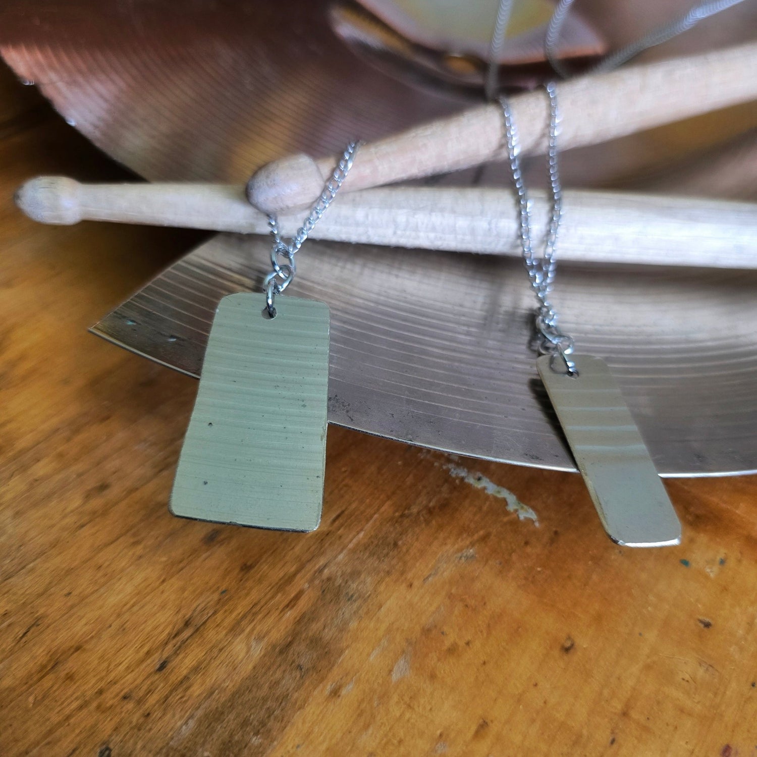 2 dog tag style upcycled cymbal piece necklaces on drumsticks and a broken cymbal 