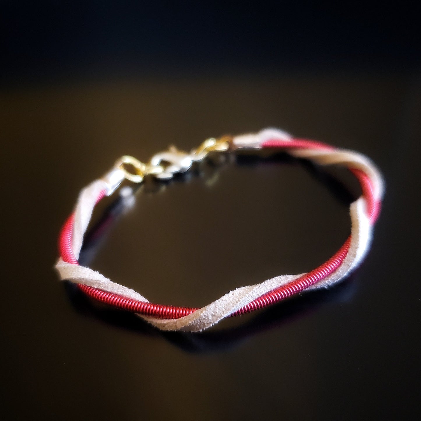 closeup of a harp string and suede  bracelet on a black background