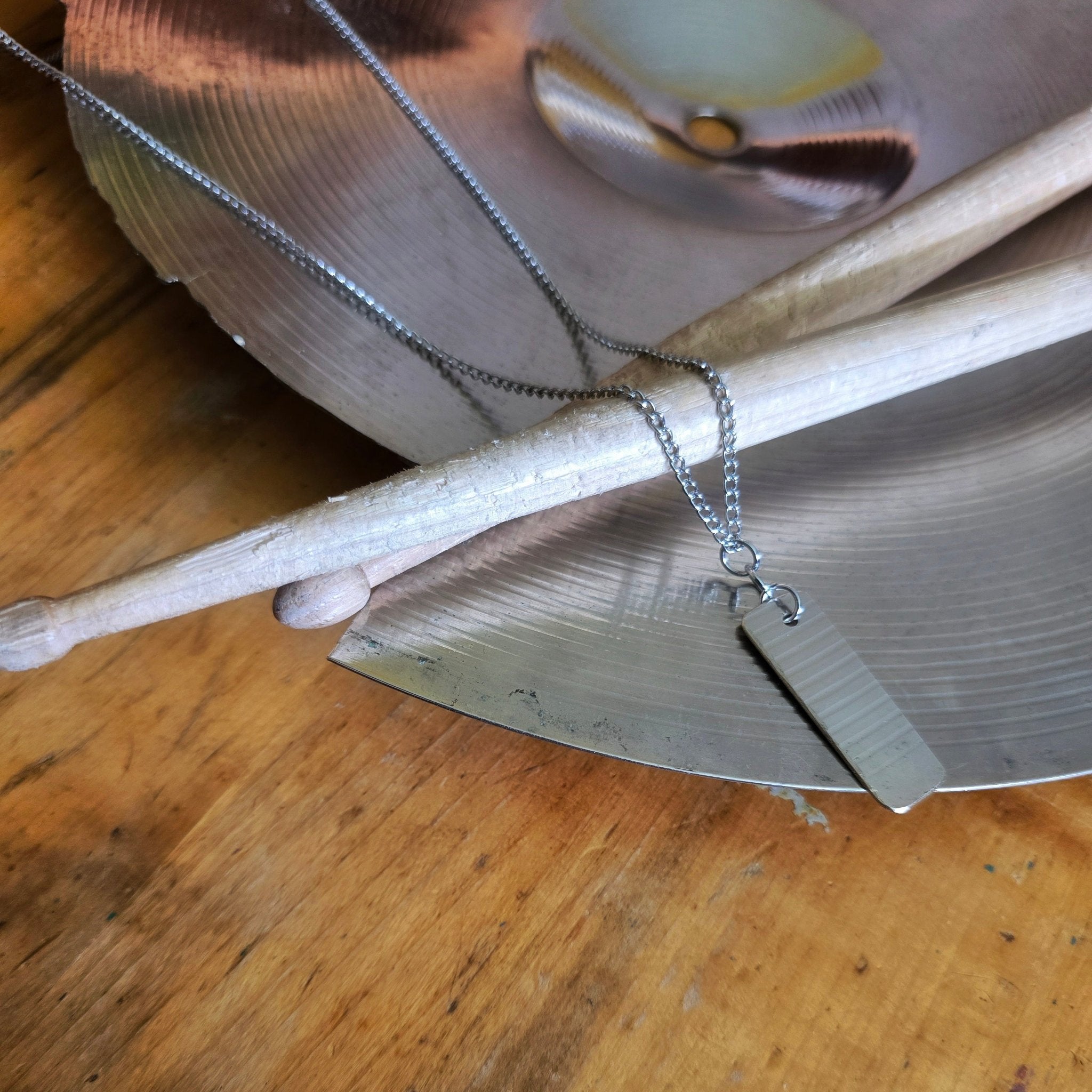 dog tag style upcycled cymbal piece necklace on drumsticks and a broken cymbal 