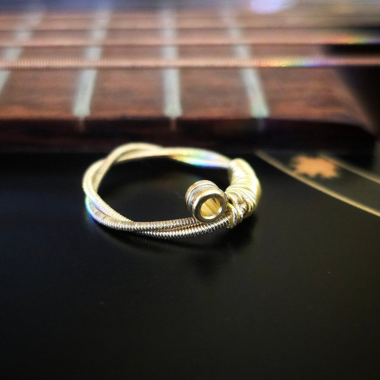 gold coloured upcycled guitar string ring sitting in front of the neck of a black guitar