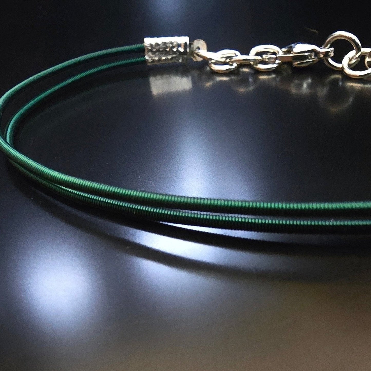 close-up of upcycled green harp string clasp bracelet on black background