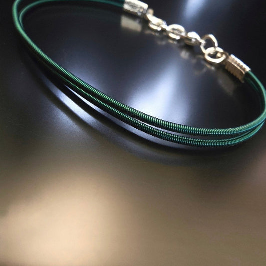 upcycled green harp string clasp bracelet on black background