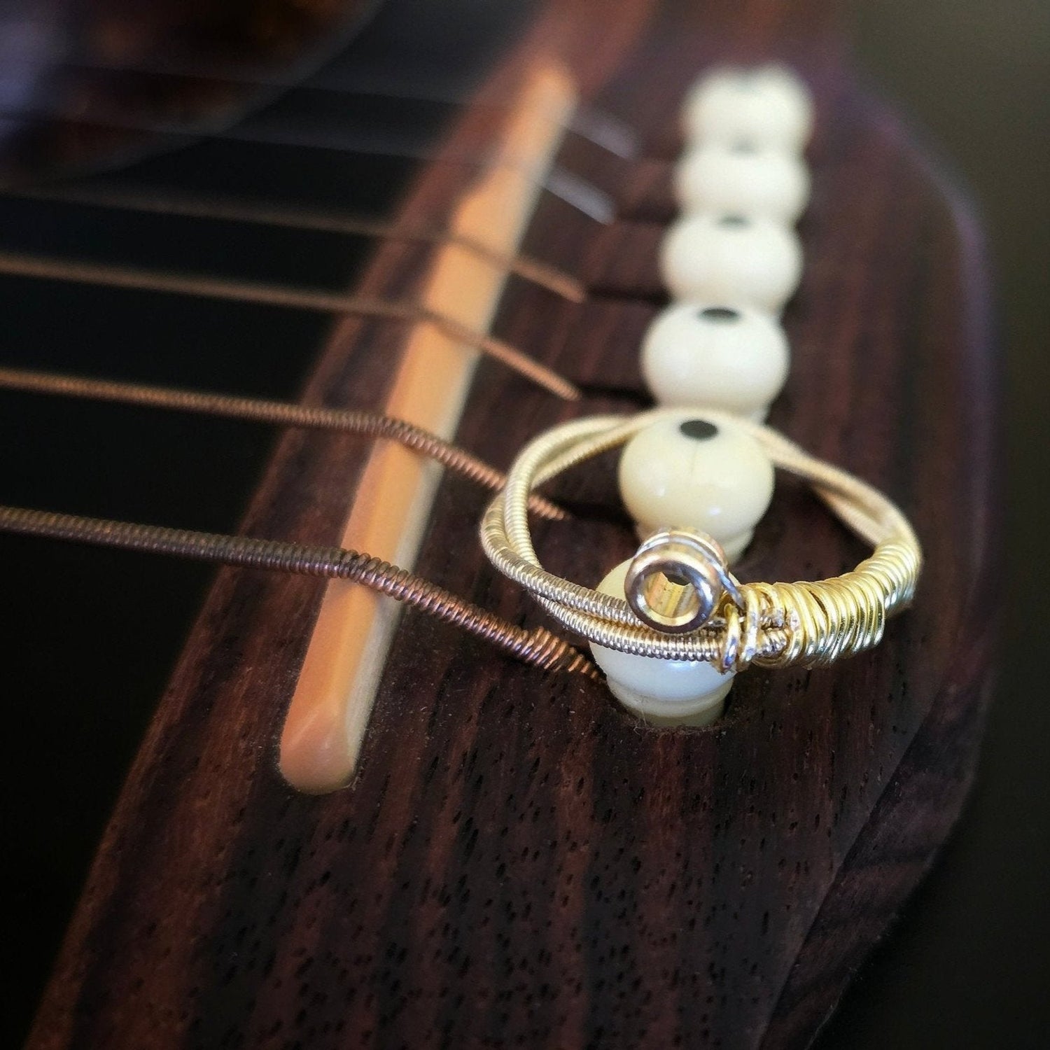 gold coloured upcycled guitar string ring sitting on the ned of the neck of a black guitar