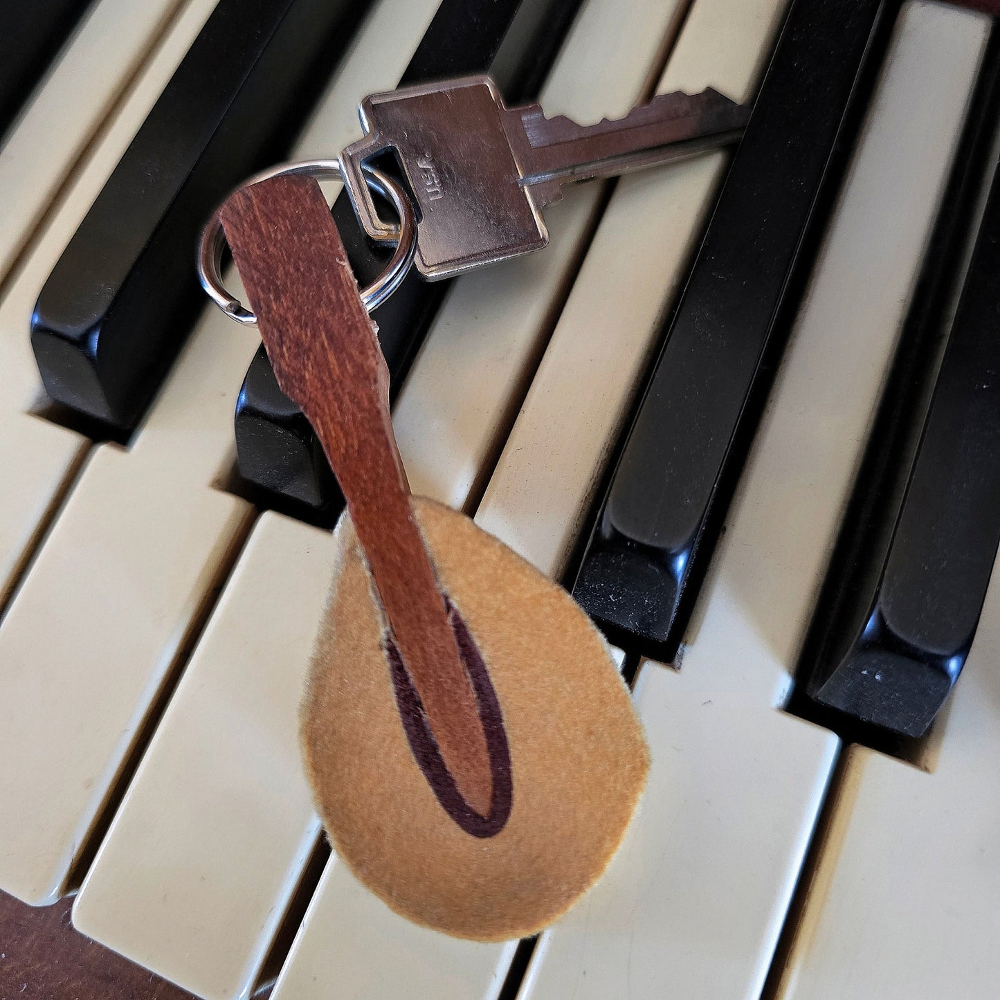 upcycled piano hammer keychain with silver key on black and white keyboard