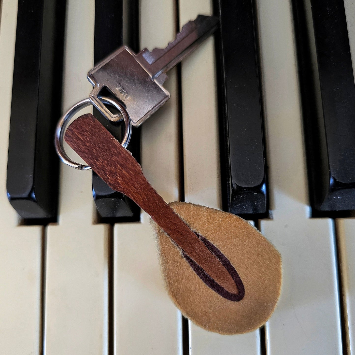 upcycled piano hammer keychain with silver key on black and white keyboard